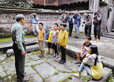 一位老人正在为孩子们讲述土楼故事,摄影师在抓取镜头.